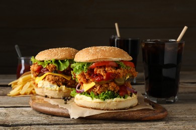 Photo of Delicious burgers with crispy chicken patty, french fries and soda drinks on wooden table