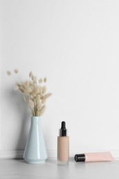 Photo of Skin foundation and dried reeds near white wall. Makeup product