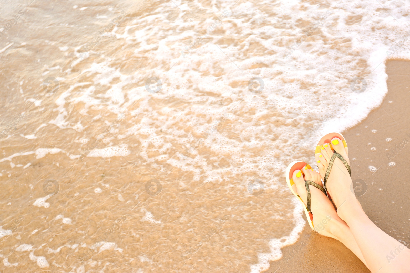 Photo of Closeup of woman with stylish flip flops on sand near sea, space for text. Beach accessories