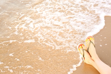 Photo of Closeup of woman with stylish flip flops on sand near sea, space for text. Beach accessories