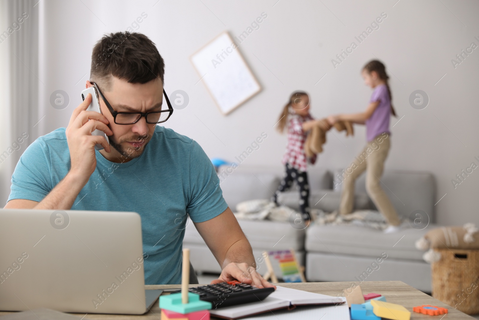 Photo of Children disturbing stressed man in living room. Working from home during quarantine