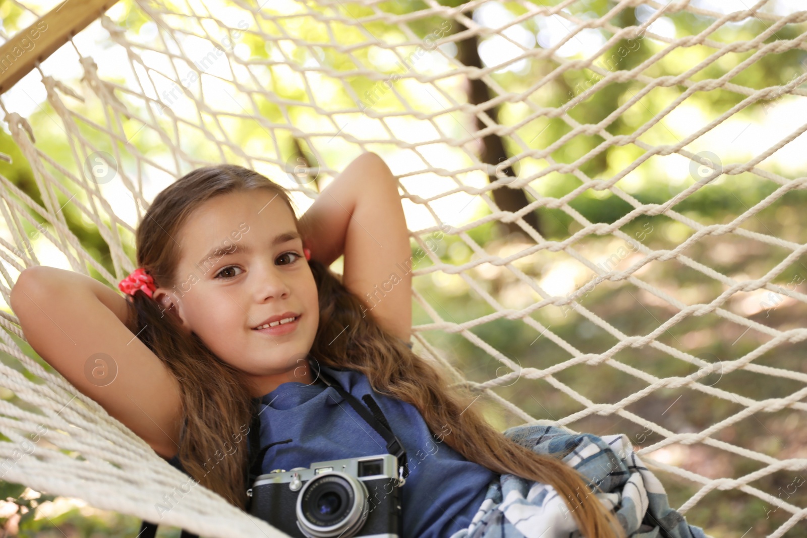 Photo of Little girl with camera in hammock outdoors. Summer camp