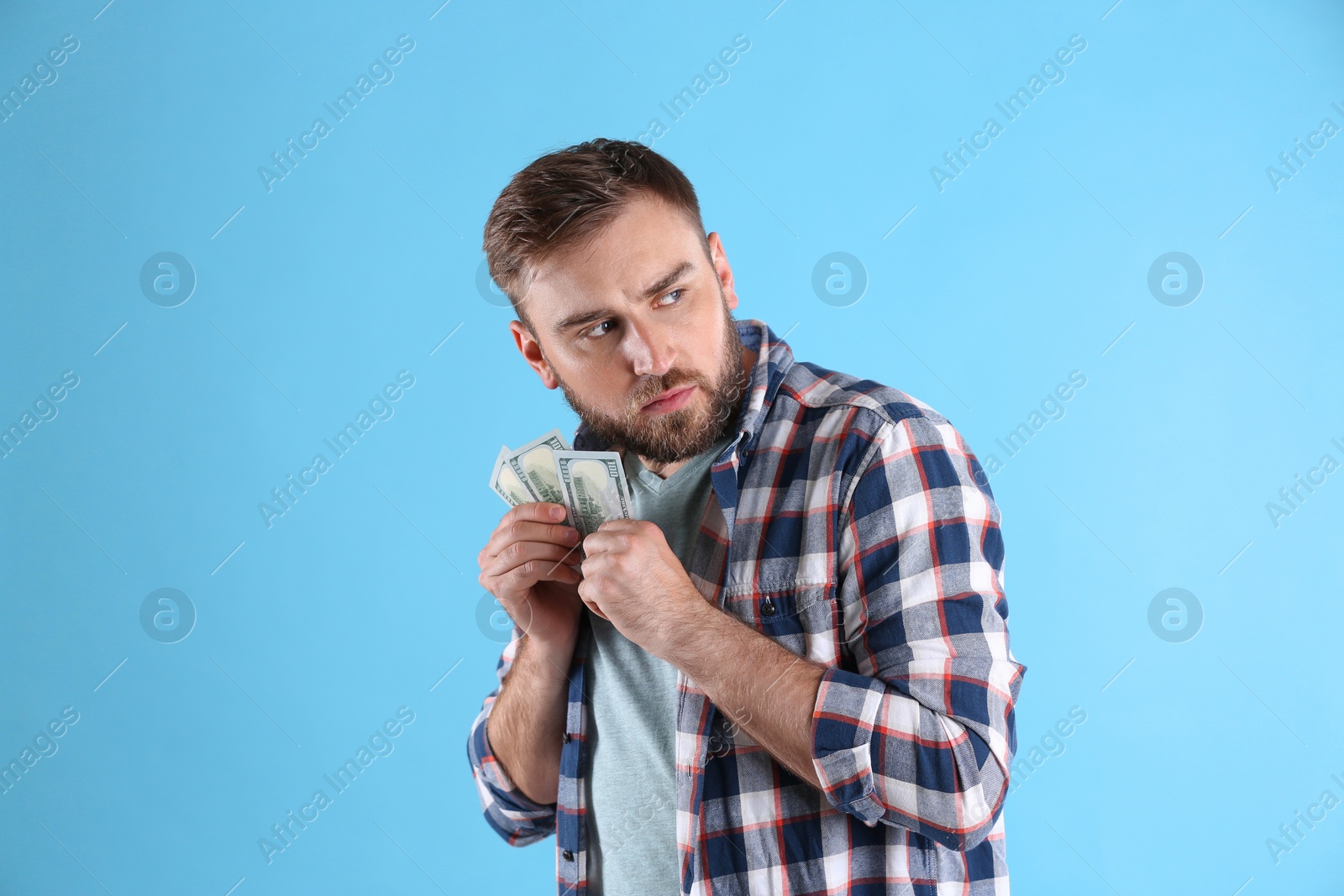 Photo of Greedy young man hiding money on light blue background