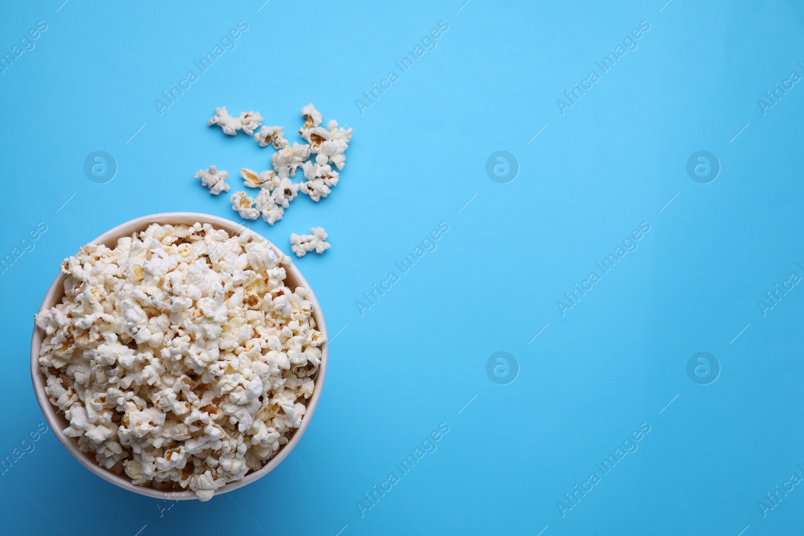 Photo of Paper bucket with delicious popcorn on light blue background, flat lay. Space for text