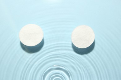 Image of Cotton pads in micellar water on light blue background, top view
