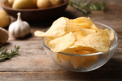 Photo of Bowl of crispy potato chips on wooden table. Space for text