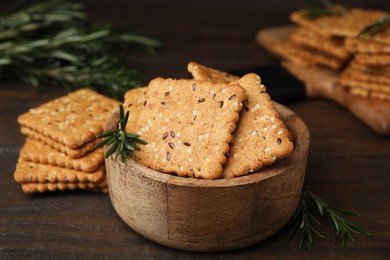Photo of Cereal crackers with flax, sesame seeds and rosemary in bowl on wooden table, closeup