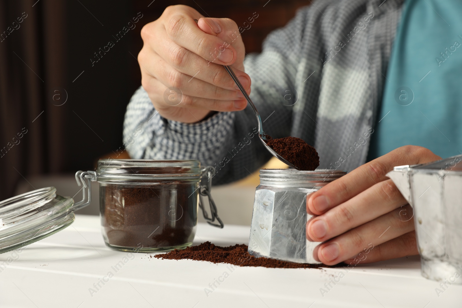 Photo of Man putting ground coffee into moka pot at white wooden table indoors, closeup
