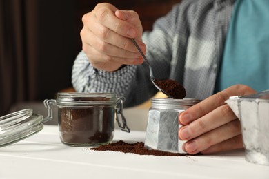 Man putting ground coffee into moka pot at white wooden table indoors, closeup