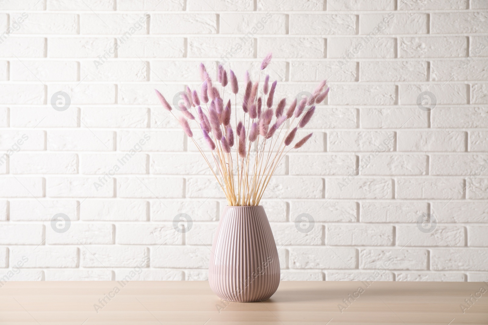 Photo of Dried flowers in vase on table against white brick wall