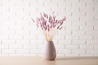 Dried flowers in vase on table against white brick wall