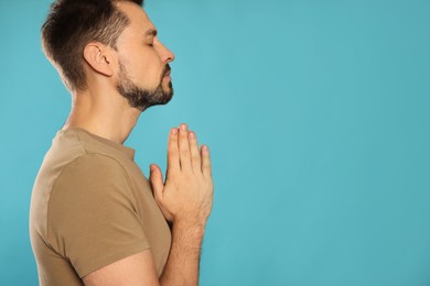 Man with clasped hands praying on turquoise background. Space for text