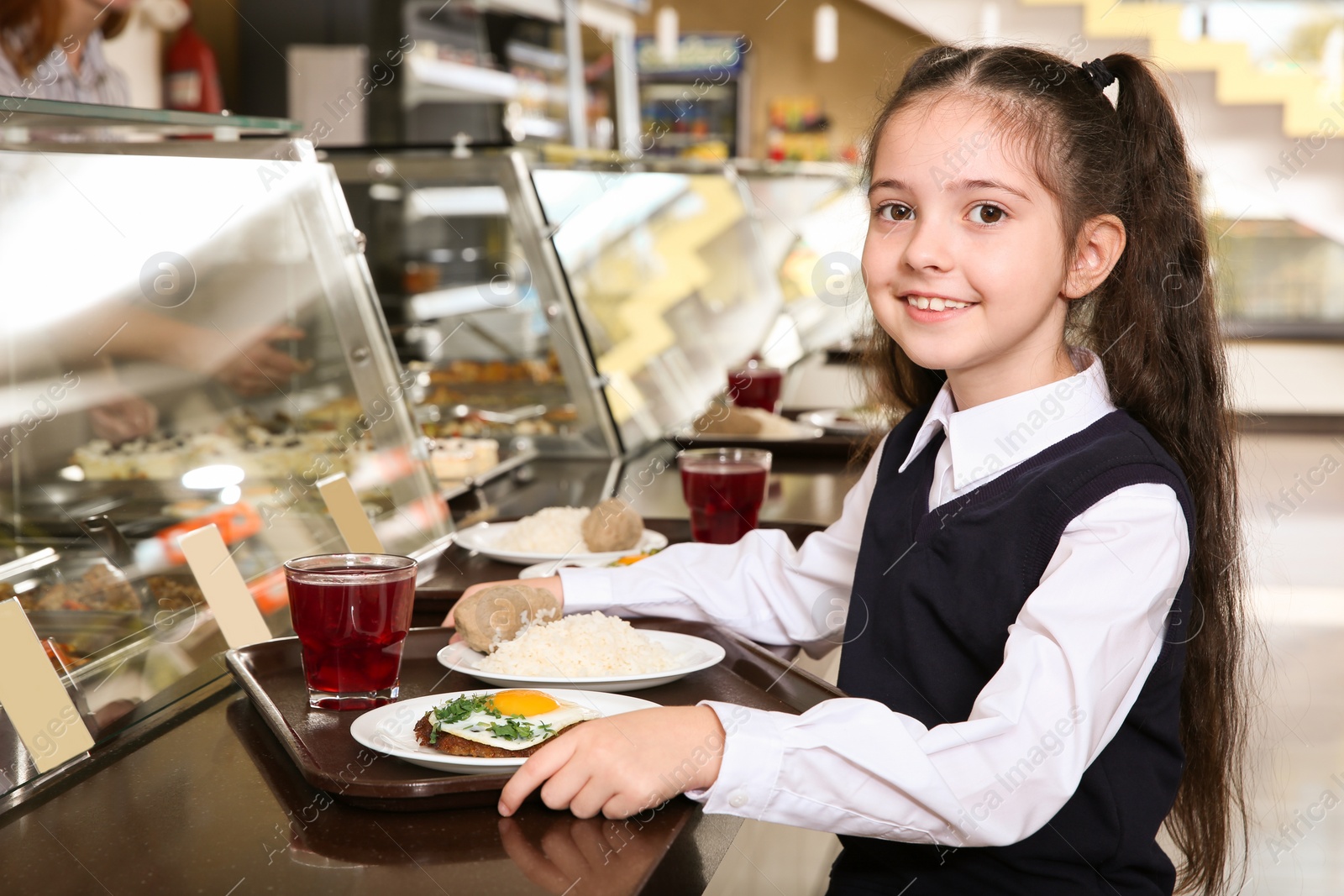 Photo of Cute girl near serving line with healthy food in school canteen