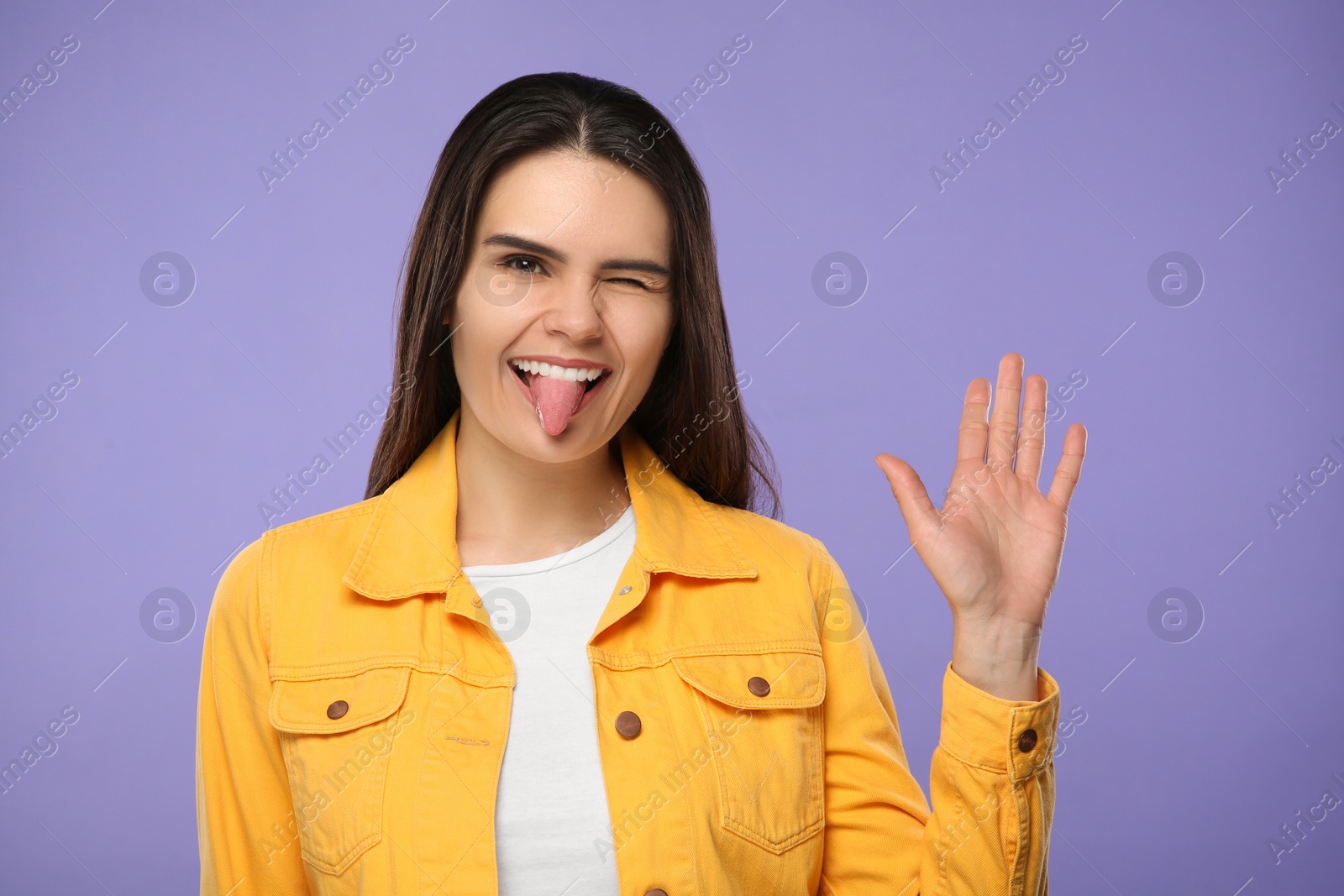 Photo of Happy young woman showing her tongue on purple background