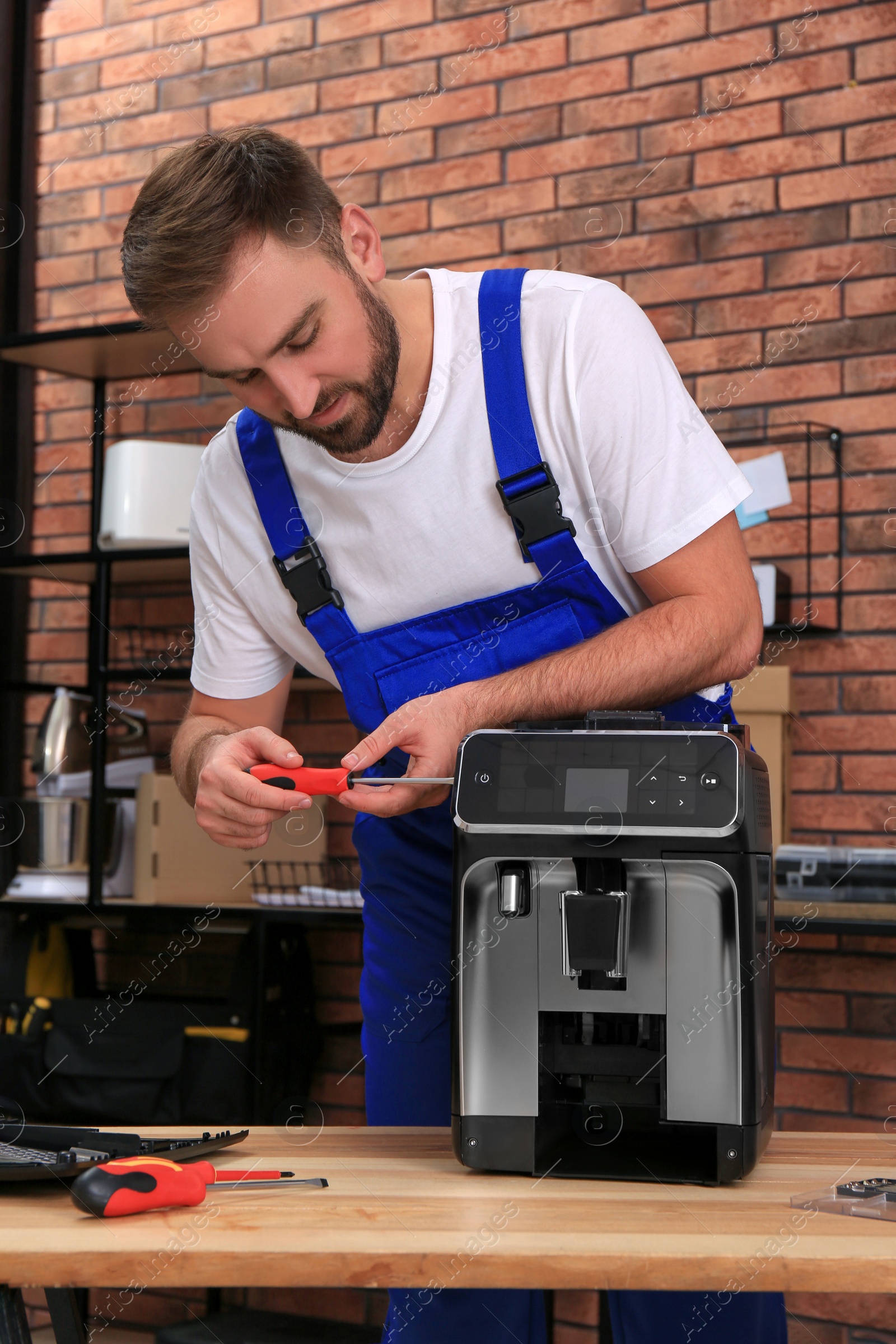 Photo of Repairman with screwdriver fixing coffee machine at table indoors