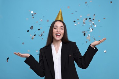 Photo of Happy woman in party hat throwing confetti on light blue background