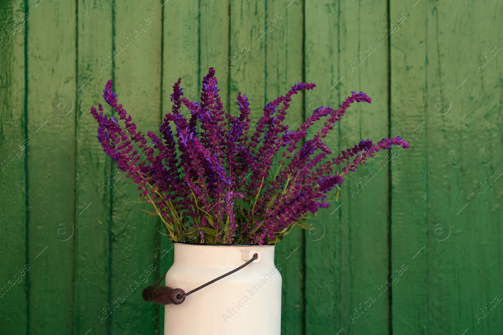 Photo of Beautiful bouquet with field flowers in can near green wooden wall