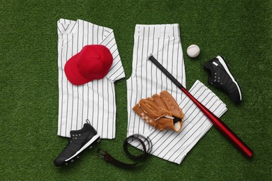 Photo of Baseball uniform and other sports equipment on artificial grass, flat lay