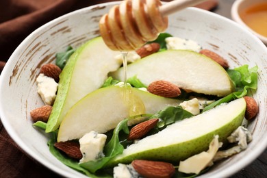 Photo of Pouring honey from dipper onto delicious pear salad in bowl, closeup