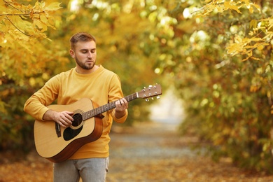 Young man playing guitar in autumn park