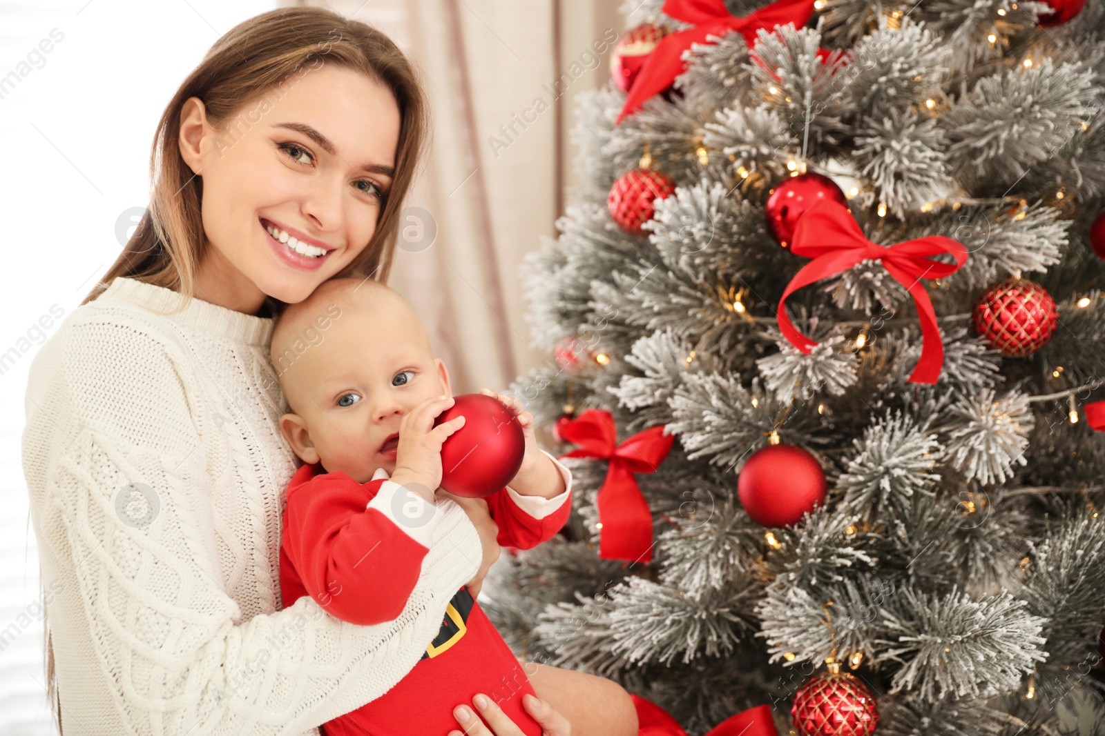 Photo of Happy mother with cute baby near Christmas tree at home