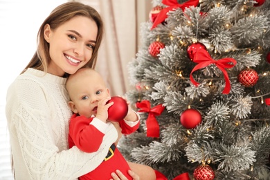 Happy mother with cute baby near Christmas tree at home
