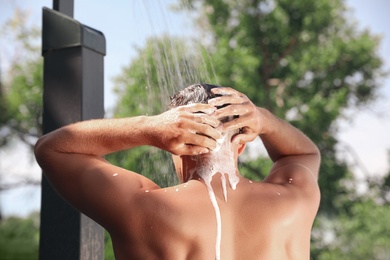 Photo of Man washing hair in outdoor shower on summer day