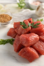 Photo of Cooking delicious goulash. Raw beef meat with parsley on white marble table, closeup