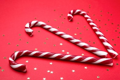 Photo of Delicious Christmas candy canes and confetti on red background, closeup