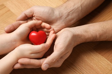 Man and kid holding red heart in hands at wooden table, closeup