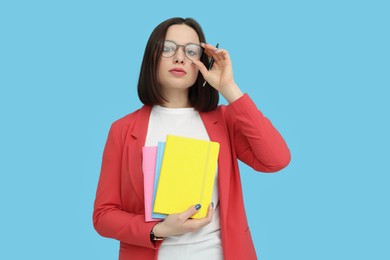 Young intern with notebooks and pen on light blue background