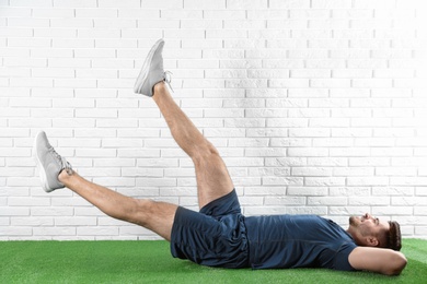 Handsome young man in sportswear doing scissors exercise on artificial green lawn near brick wall