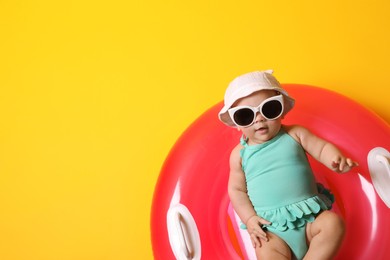 Cute little baby in sunglasses with inflatable ring on yellow background, space for text