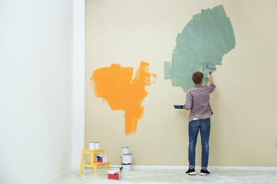 Young man painting wall indoors, space for text. Home repair