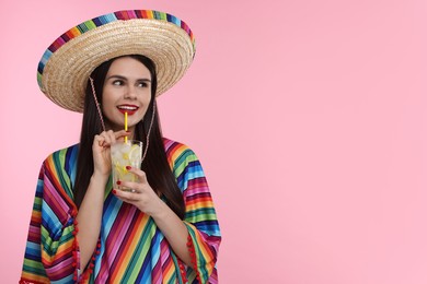 Young woman in Mexican sombrero hat and poncho holding cocktail on pink background. Space for text