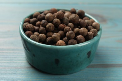 Photo of Aromatic allspice pepper grains in bowl on light blue wooden table, closeup