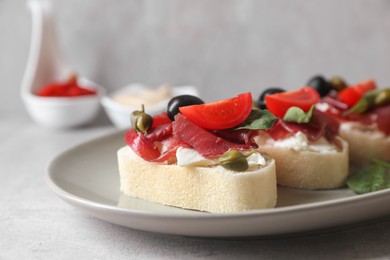 Photo of Delicious sandwiches with bresaola, cream cheese, olives and tomato on light grey table, closeup