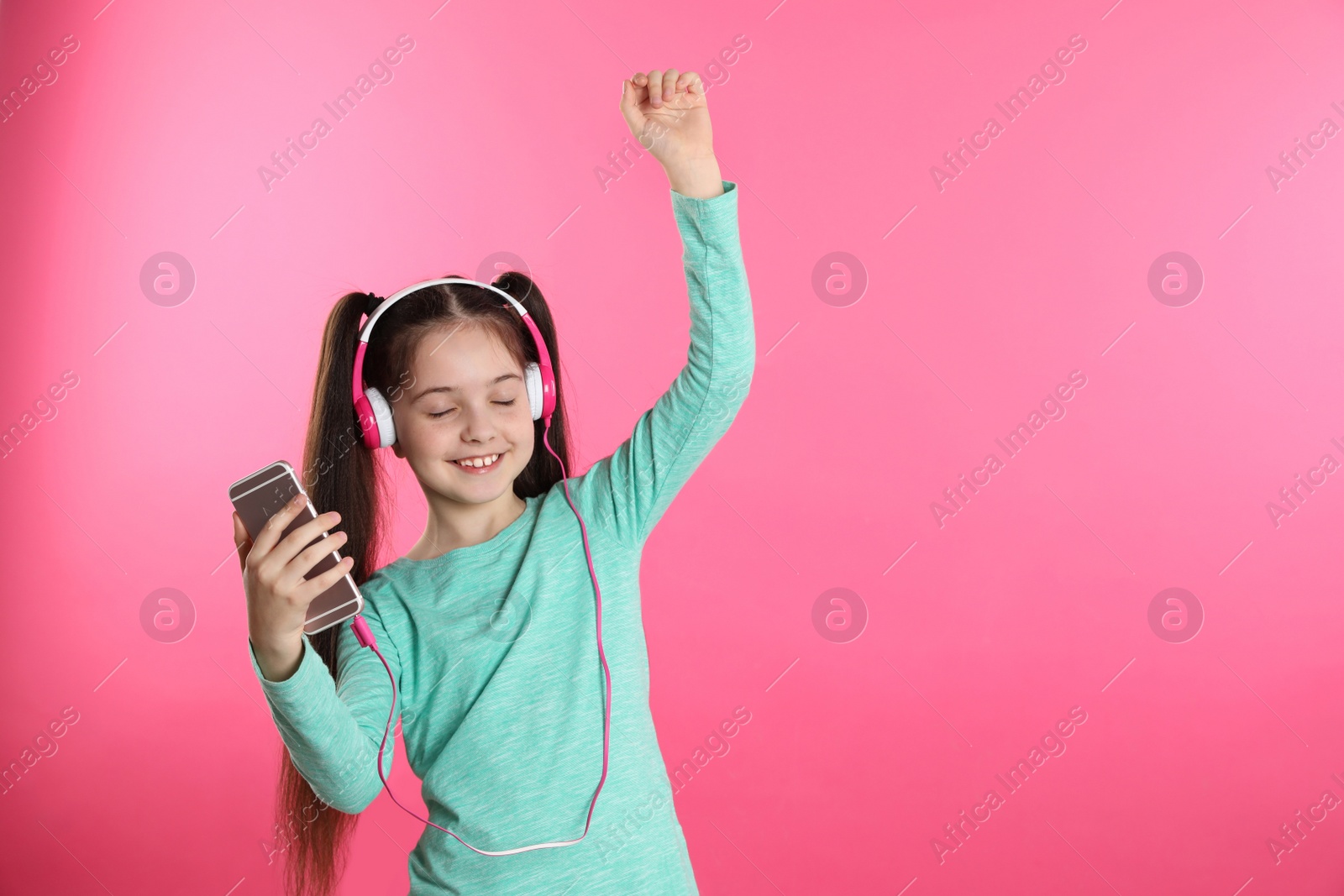Photo of Cute girl with mobile phone enjoying music in headphones on color background. Space for text