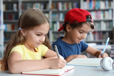 Little children writing at table with books in library reading room