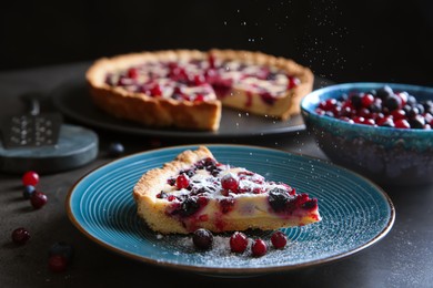 Photo of Sprinkling powdered sugar onto piece of delicious currant pie on grey table, closeup