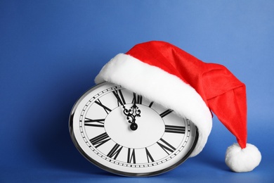 Photo of Clock with Santa hat showing five minutes until midnight on blue background. New Year countdown