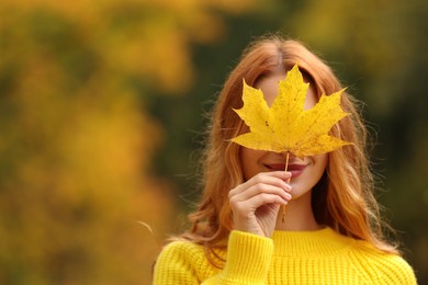 Woman covering face with autumn leaf outdoors. Space for text