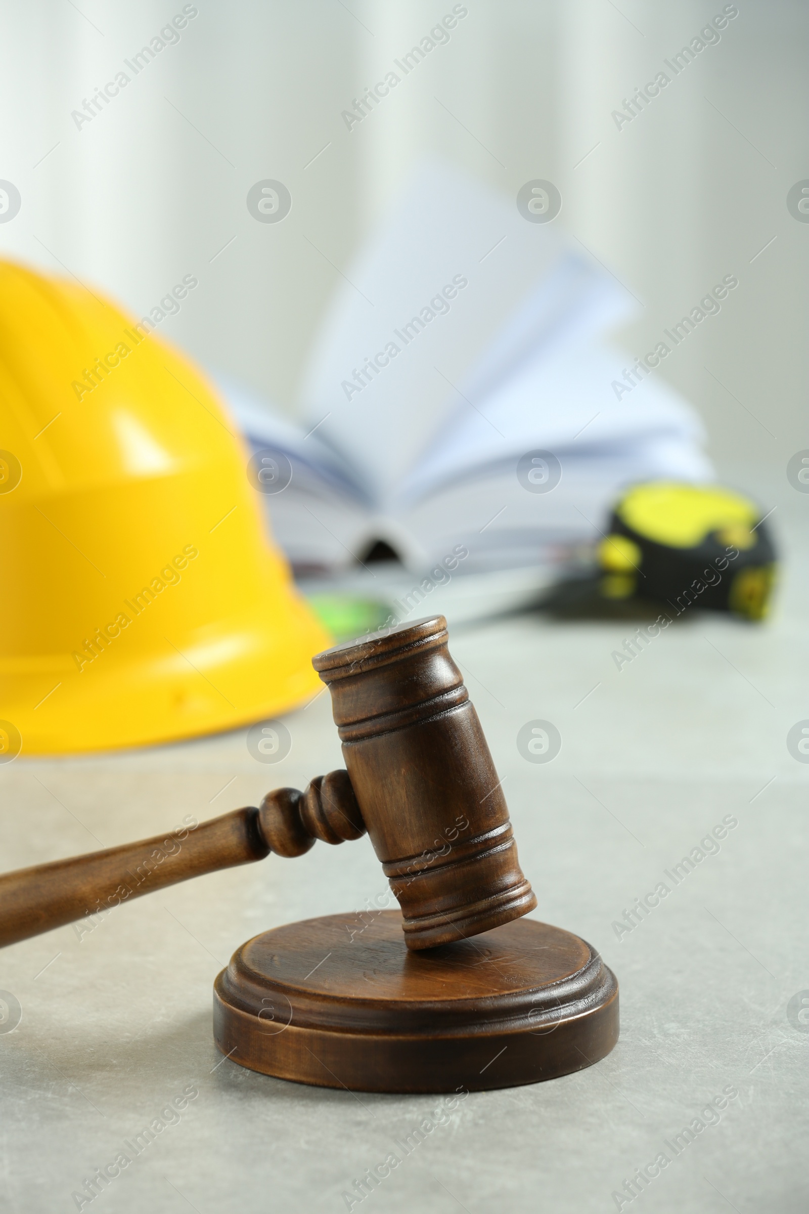 Photo of Construction and land law concepts. Judge gavel, construction helmet, tape measure and open book on light grey table