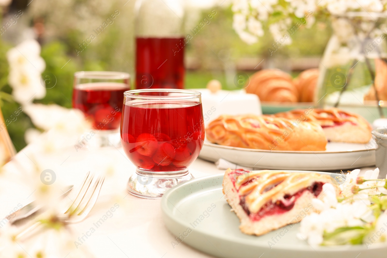 Photo of Stylish table setting with beautiful spring flowers, fruit drink and pie in garden