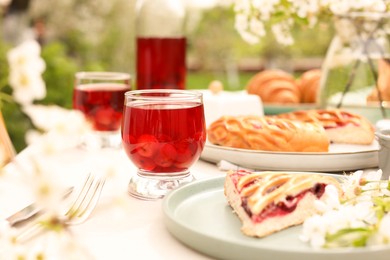 Photo of Stylish table setting with beautiful spring flowers, fruit drink and pie in garden