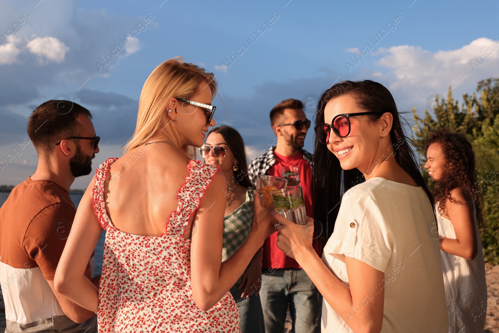 Photo of Group of friends with drinks having fun near river at summer party