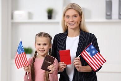 Immigration. Happy woman with her daughter holding passports and American flags indoors