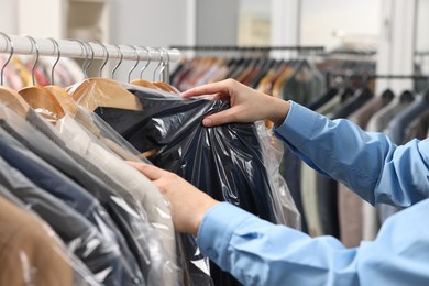 Dry-cleaning service. Woman taking jacket in plastic bag from rack indoors, closeup