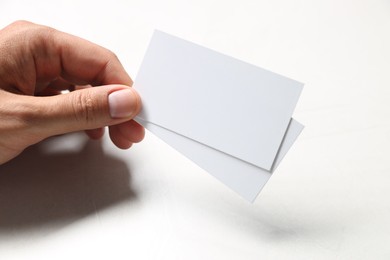 Photo of Man holding blank cards at white table, closeup. Mockup for design