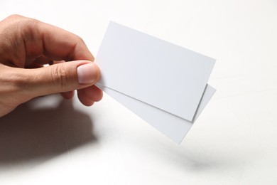 Man holding blank cards at white table, closeup. Mockup for design